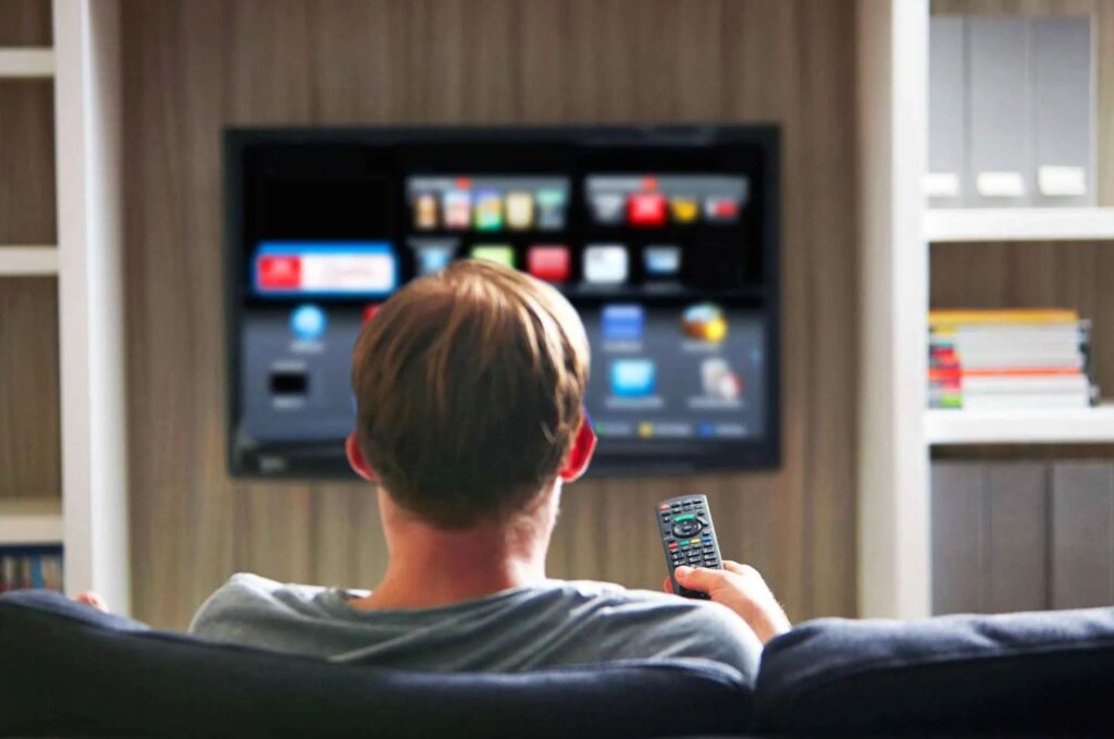 A viewer using a remote to browse a smart TV interface at home in Canada